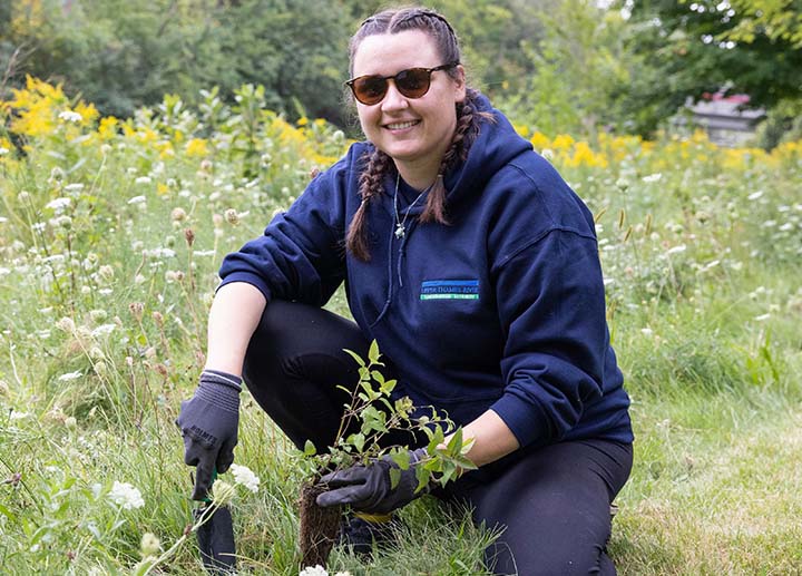 Student crouching by over grown grass and gardening